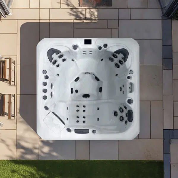 An overhead view of a square white hot tub installed on a paved patio next to a grass lawn.