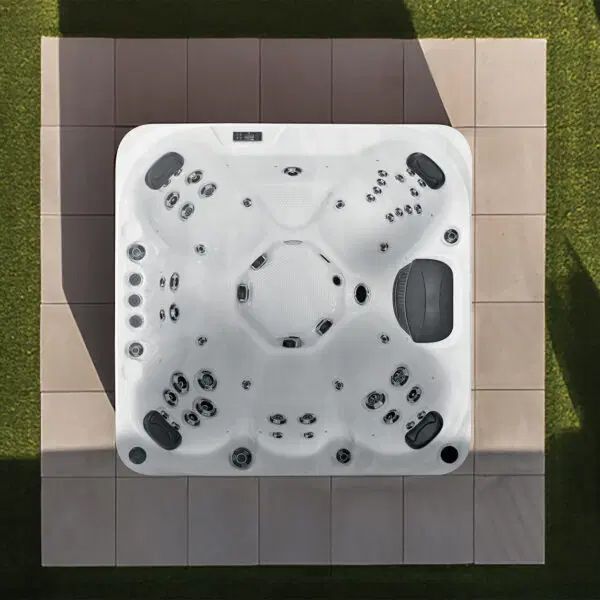 A white square hot tub with seating for four, centered on a tiled patio surrounded by green lawn, viewed from above.