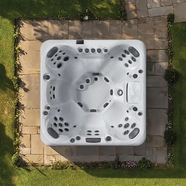 Overhead view of a white rectangular hot tub centered on a stone patio surrounded by a green lawn.