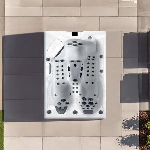 Overhead view of a rectangular white hot tub with contoured seats and jets, installed on a light-colored stone patio.