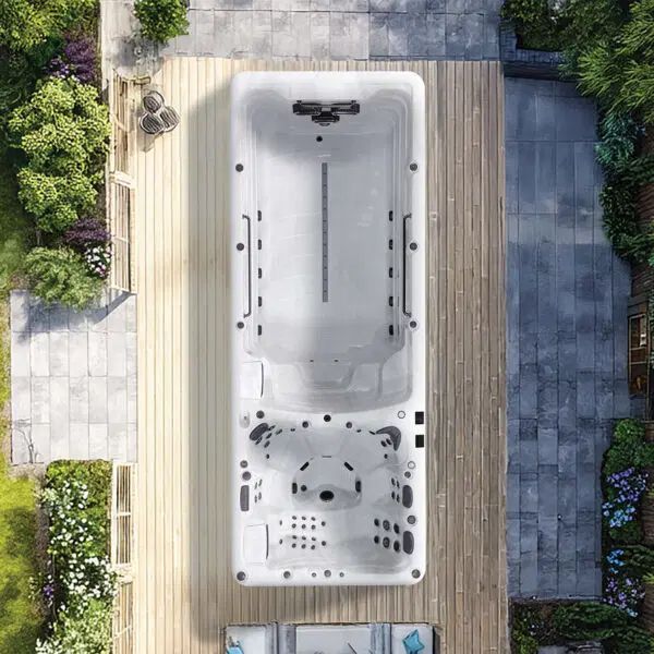 A top-down view of a rectangular swim spa with integrated seating and massage jets, installed on a wooden deck in a garden.