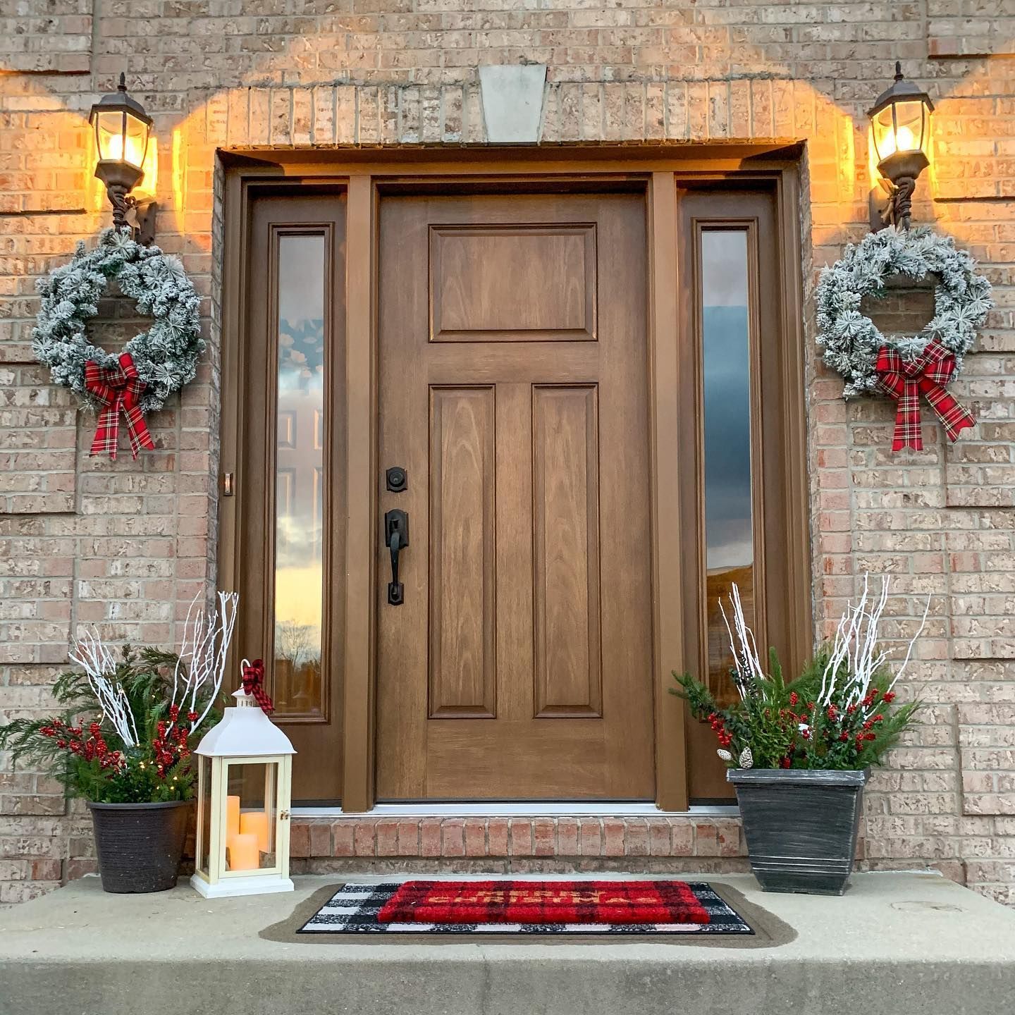 The front door of a brick house is decorated for christmas with wreaths and lanterns.