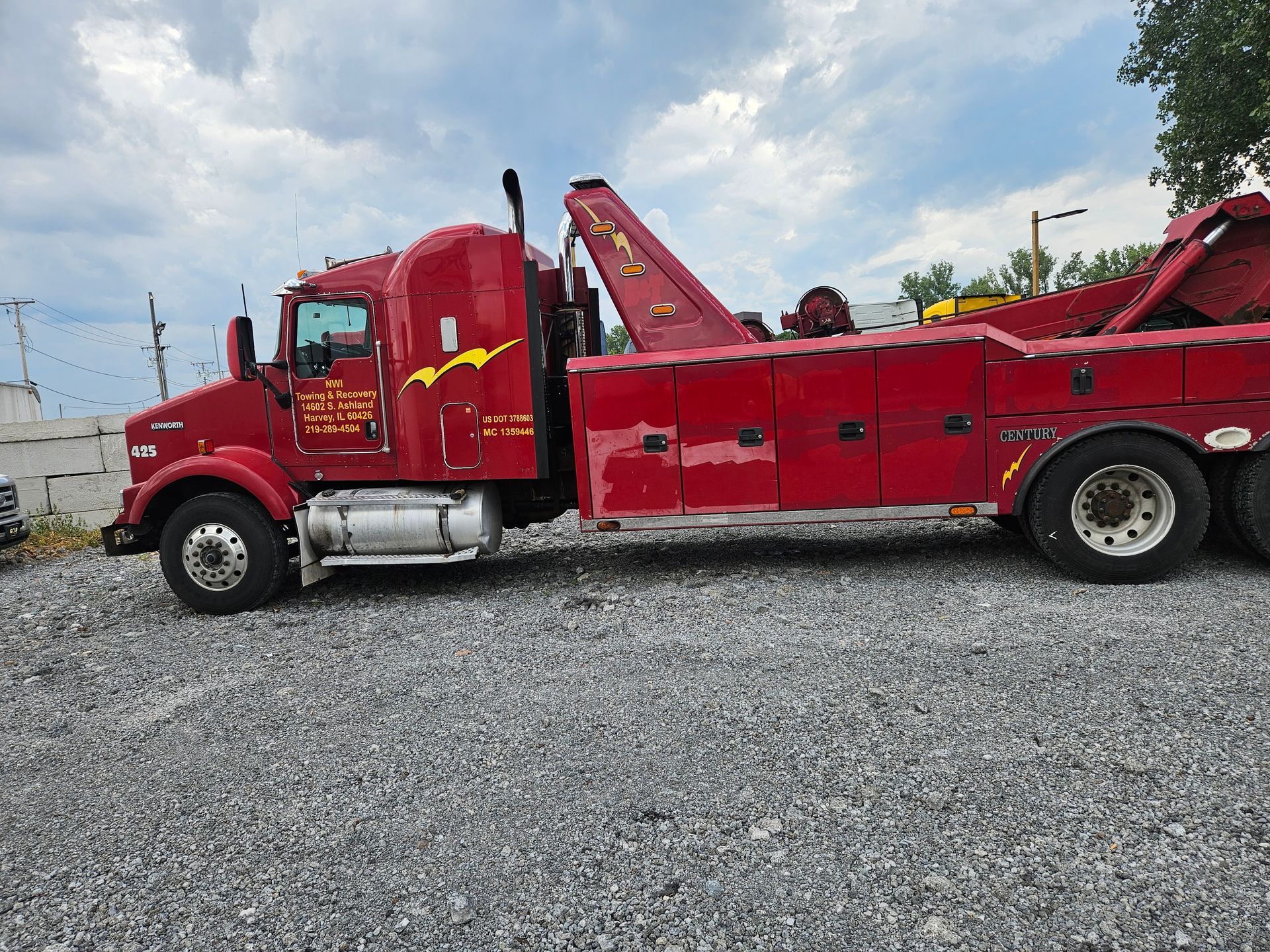 A red tow truck is parked in a gravel lot