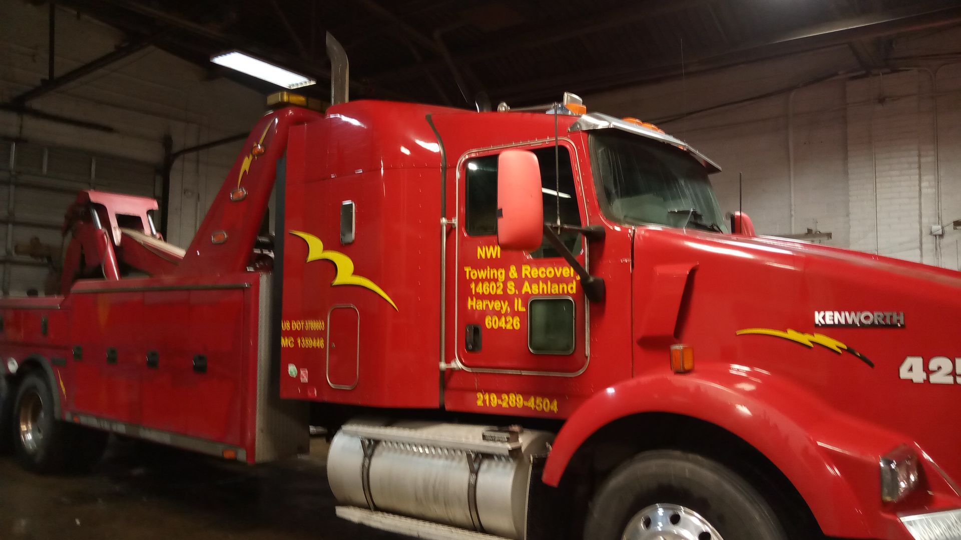 A red kenworth tow truck is parked in a garage