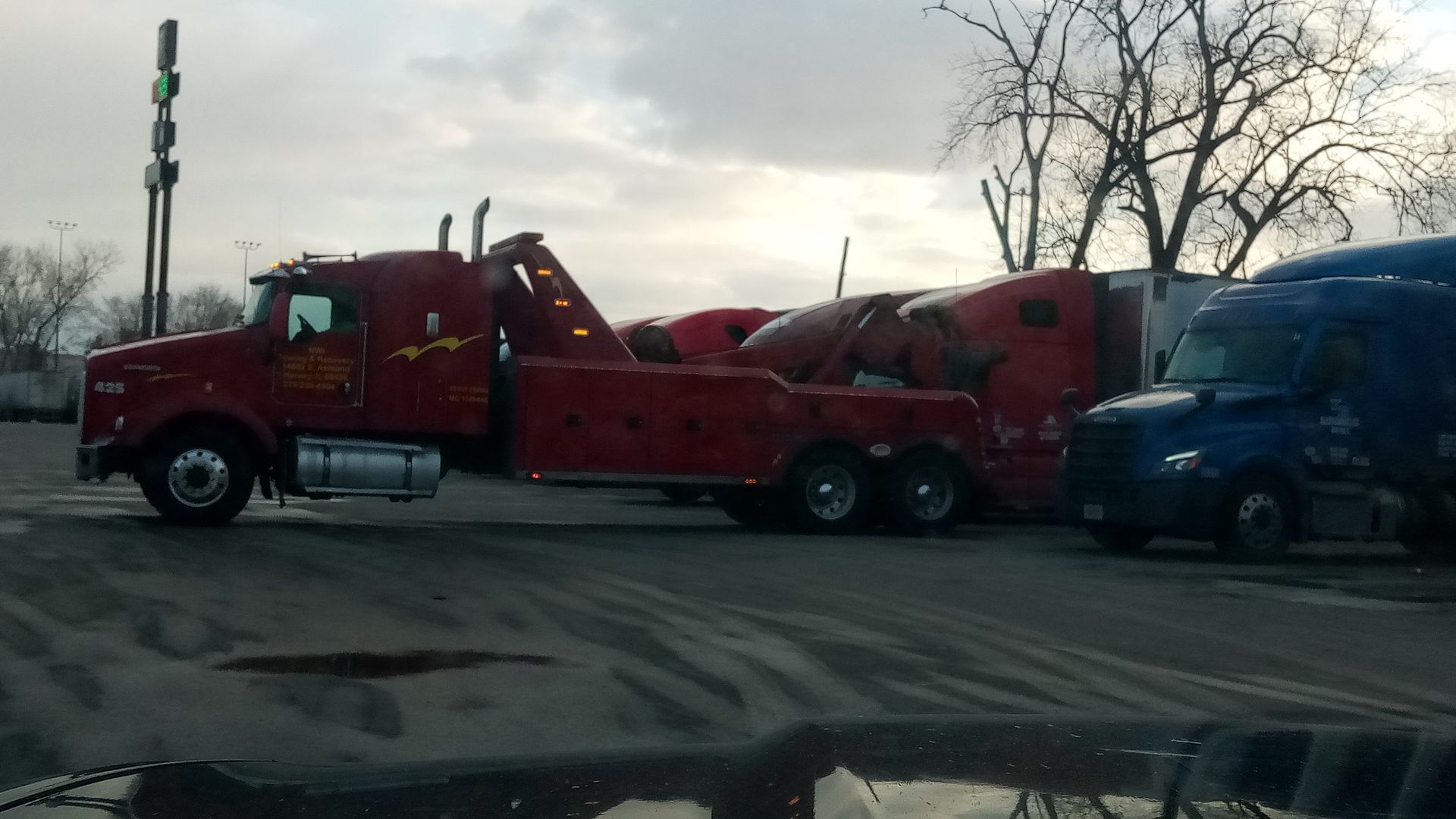 A red tow truck is parked next to a blue truck