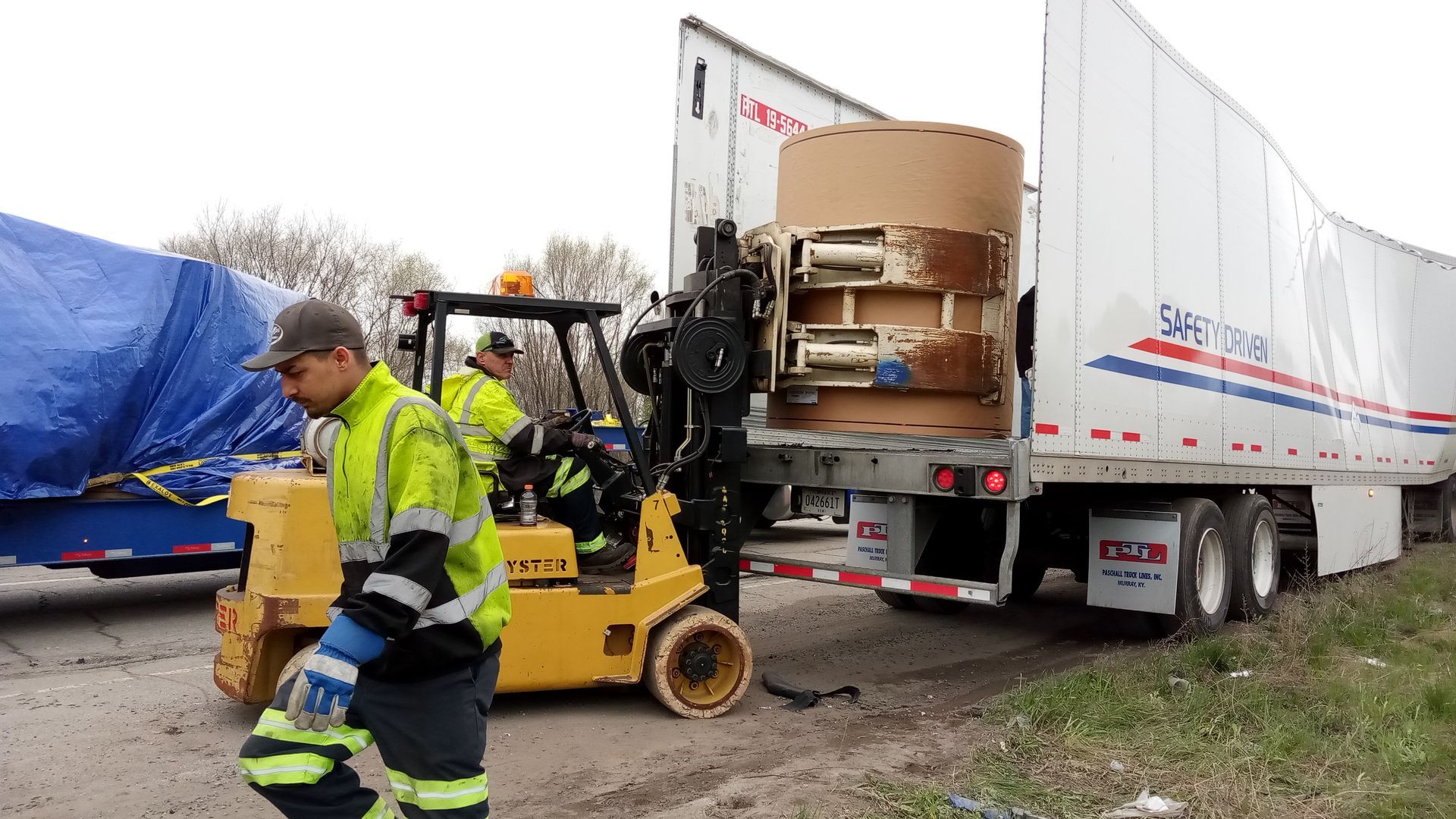 A man is standing next to a forklift in front of a semi truck.