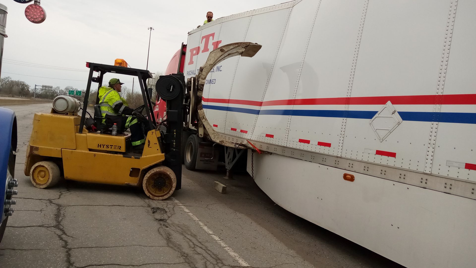 A man is driving a forklift next to a t-mobile truck