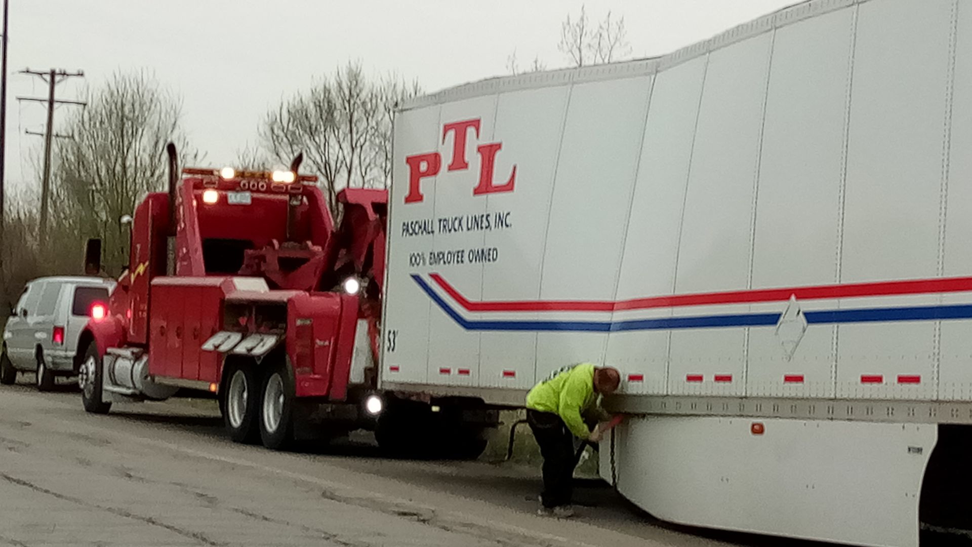 A red tow truck is towing a white trailer that says ptl on it.