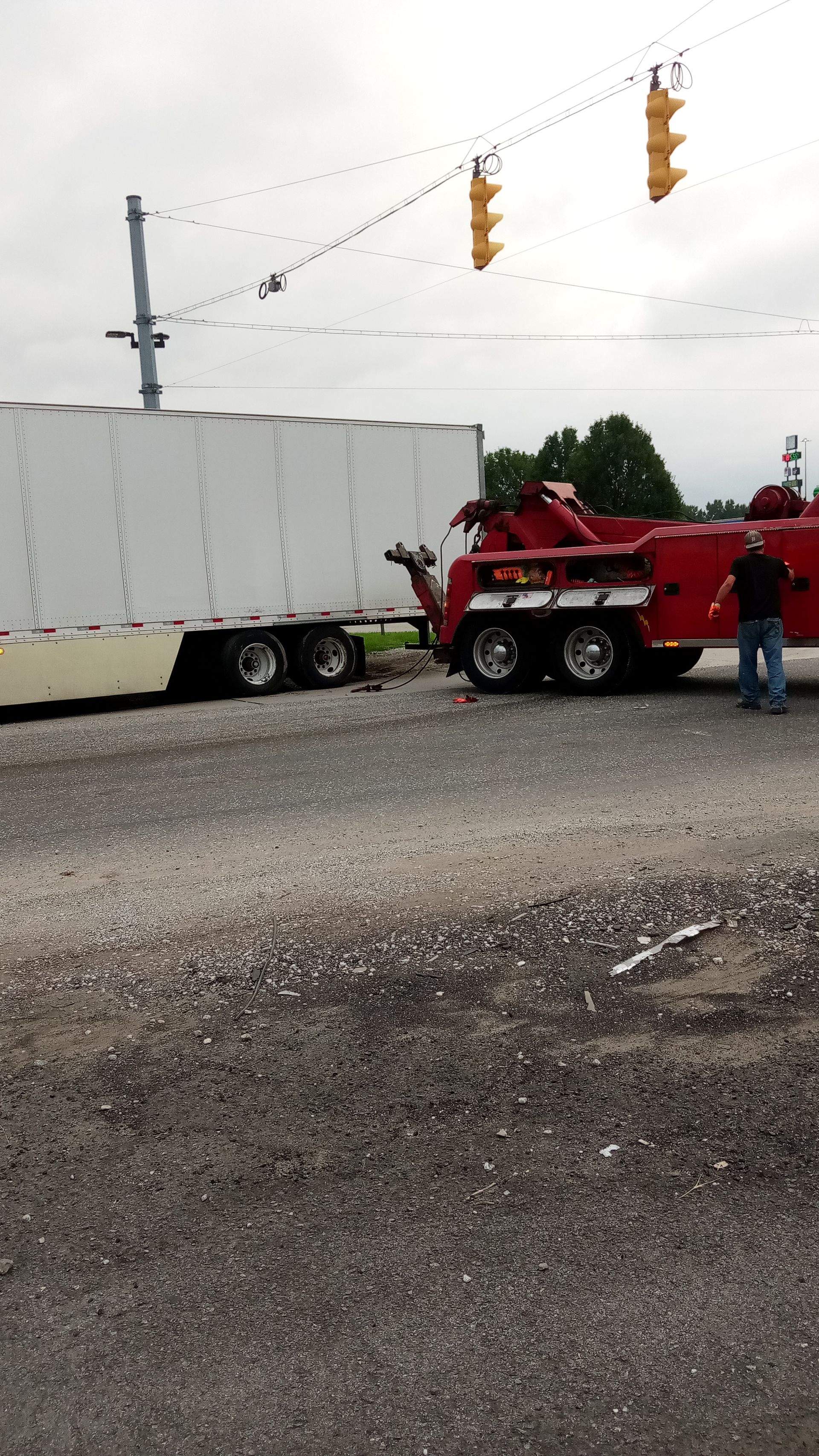 A red tow truck is towing a white trailer in a gravel lot.
