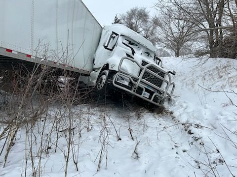 A semi truck is stuck in the snow on the side of the road.