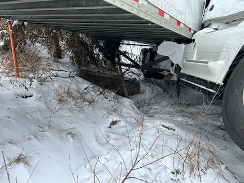 A semi truck has crashed into a tree in the snow.