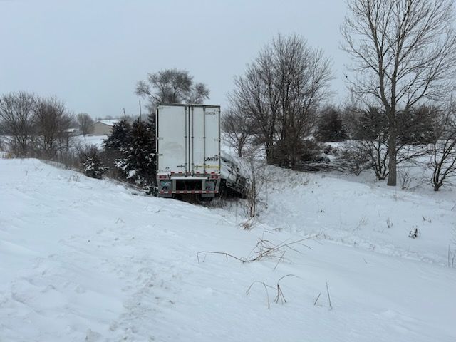 A semi truck is stuck in the snow on the side of the road.