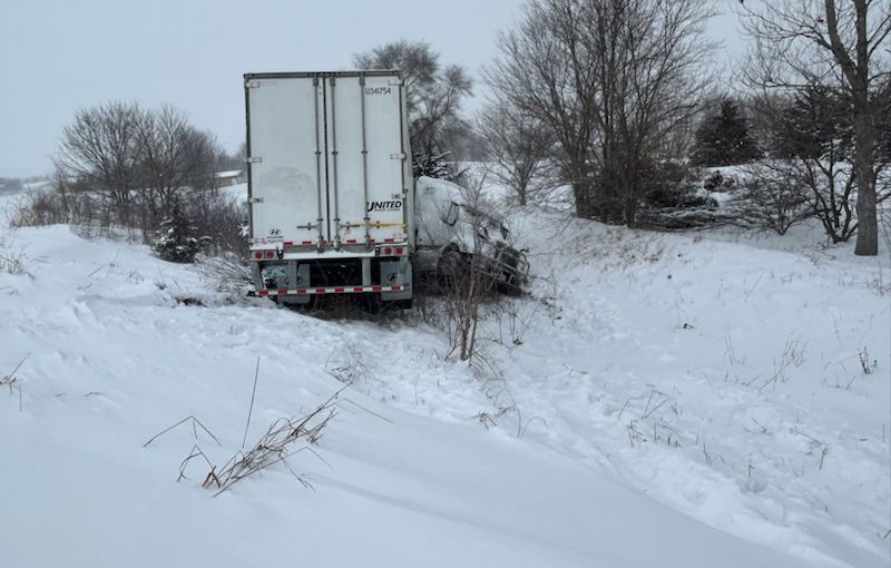 A semi truck is stuck in the snow on a snowy road.