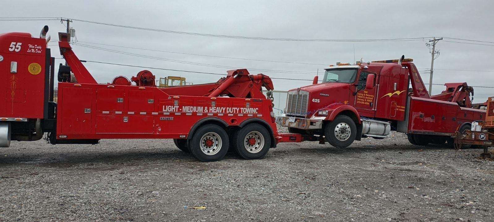 Two red tow trucks are parked next to each other in a gravel lot.