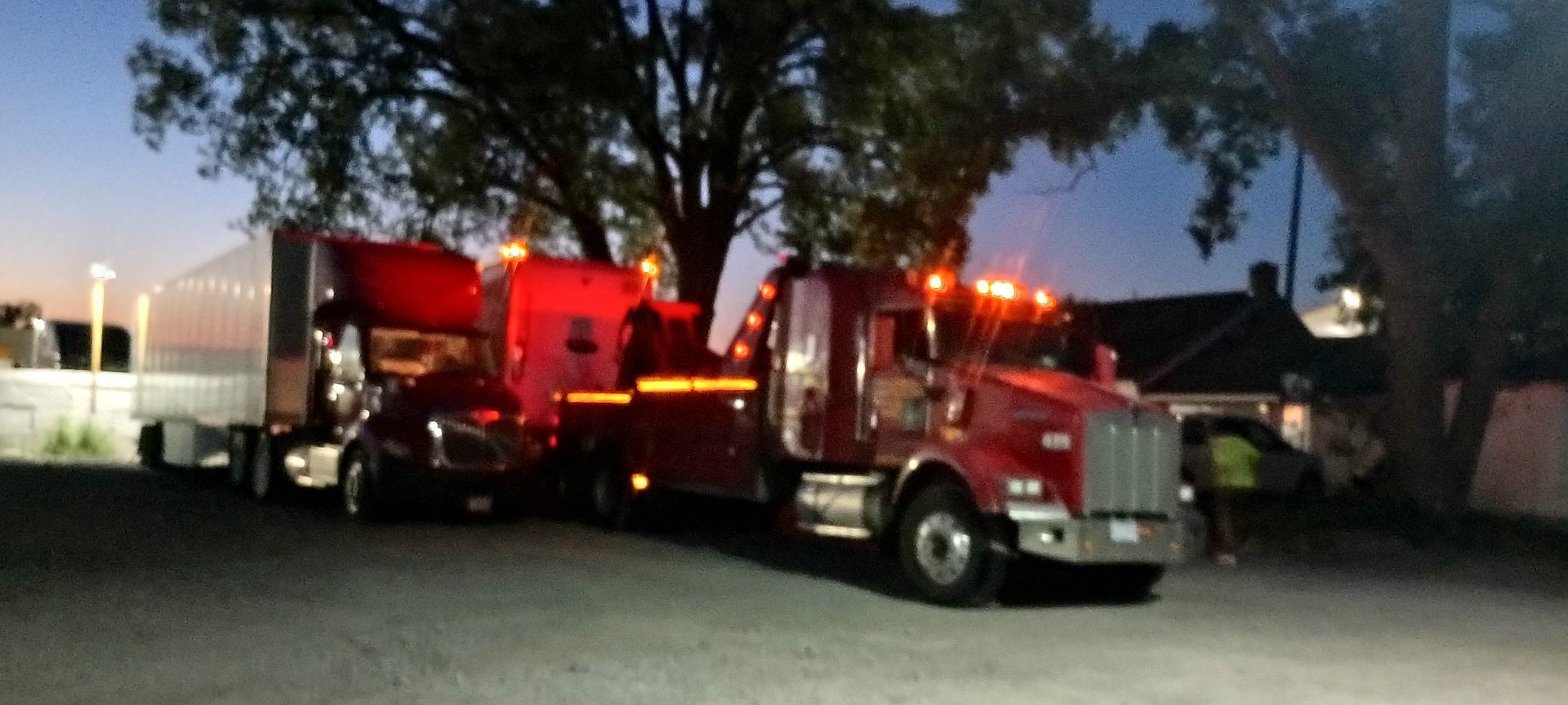 Two tow trucks are parked next to each other in a parking lot at night.