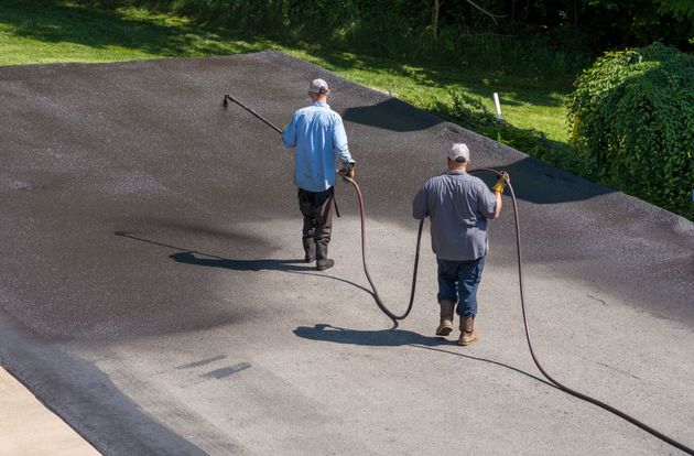 Two workers walking on a gravel path with long hoses in a grassy outdoor area