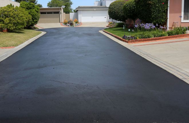 Freshly paved black driveway leading to garage doors in a suburban home