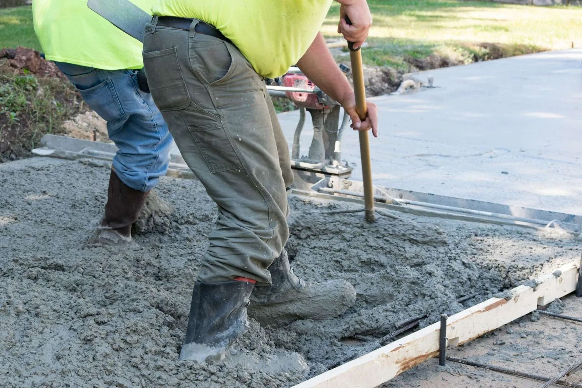 Construction workers pouring and smoothing wet concrete along a curb outdoors