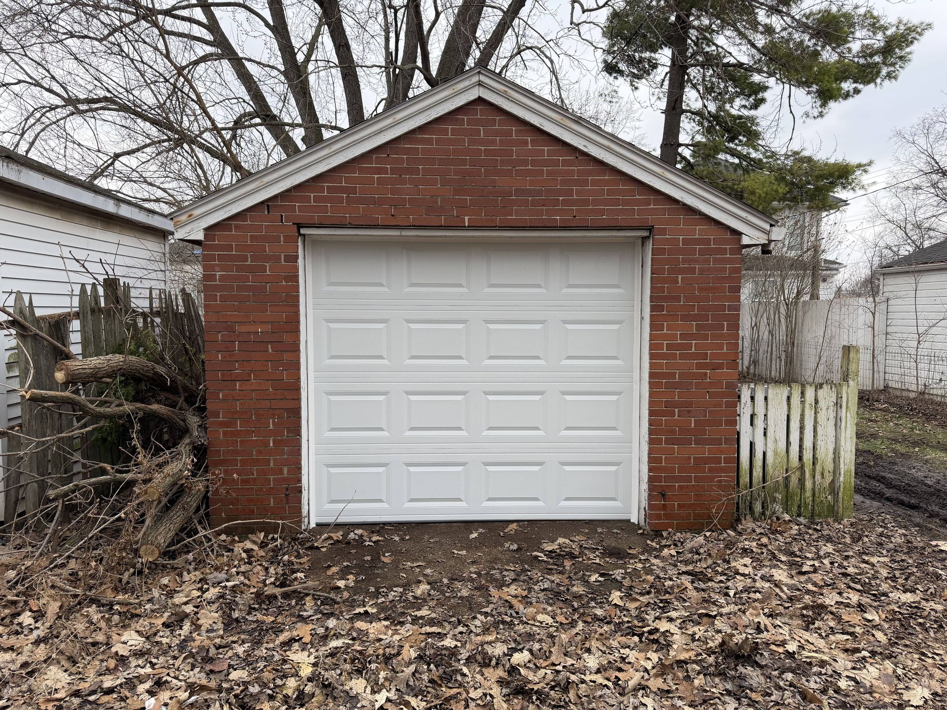 Brick garage with a white garage door, surrounded by dead leaves.