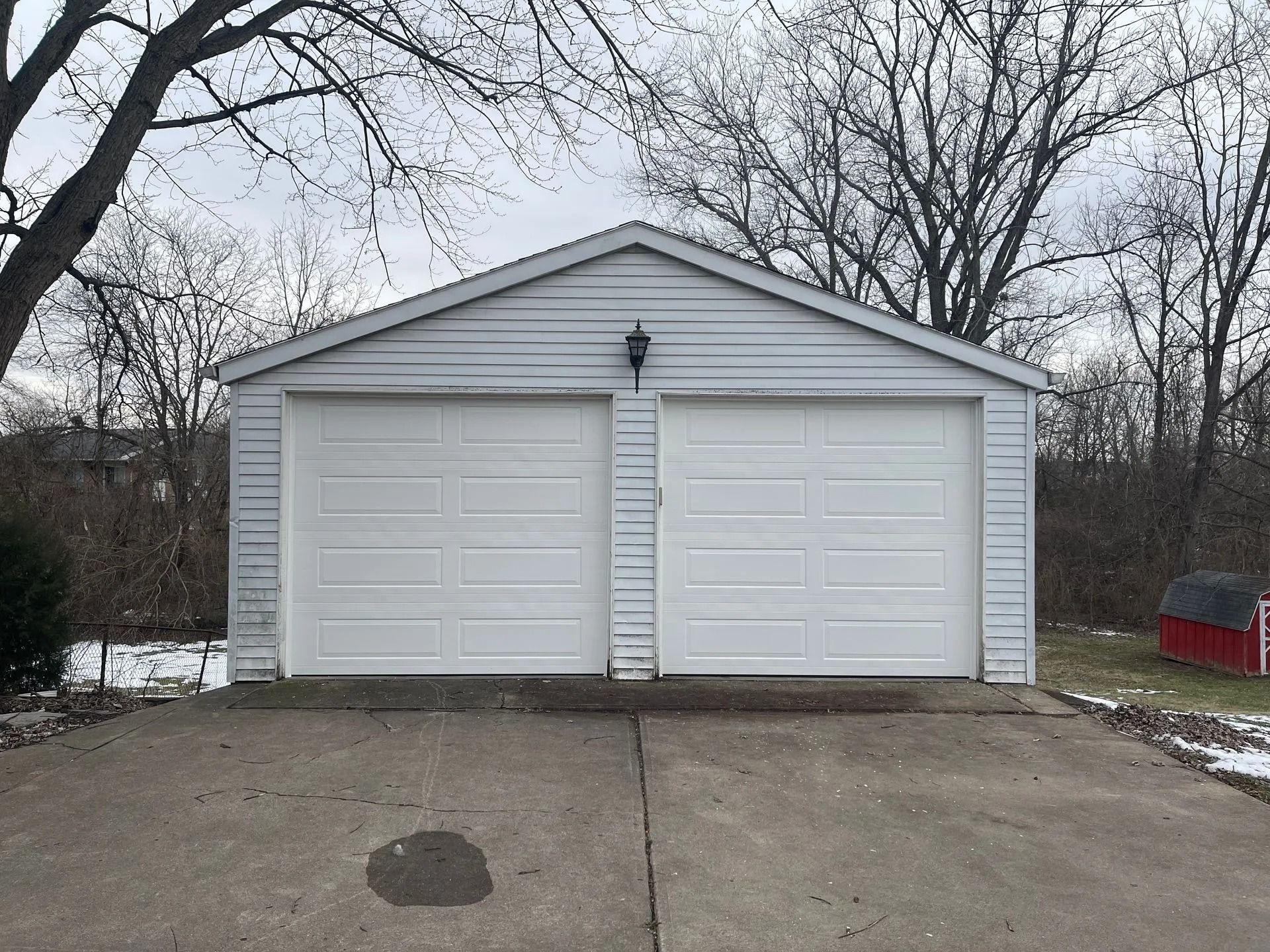 White two-car garage with closed doors, concrete driveway, and bare trees in the background.