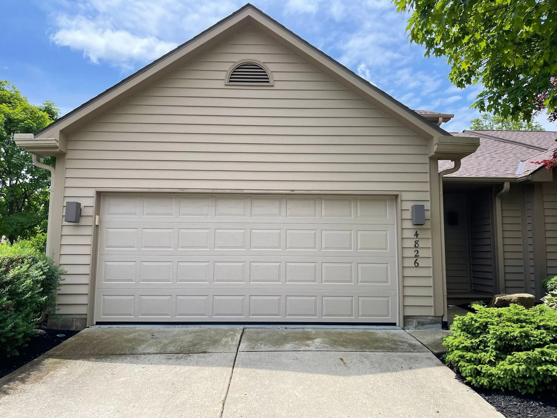 Beige garage door on a home with tan siding and a driveway.