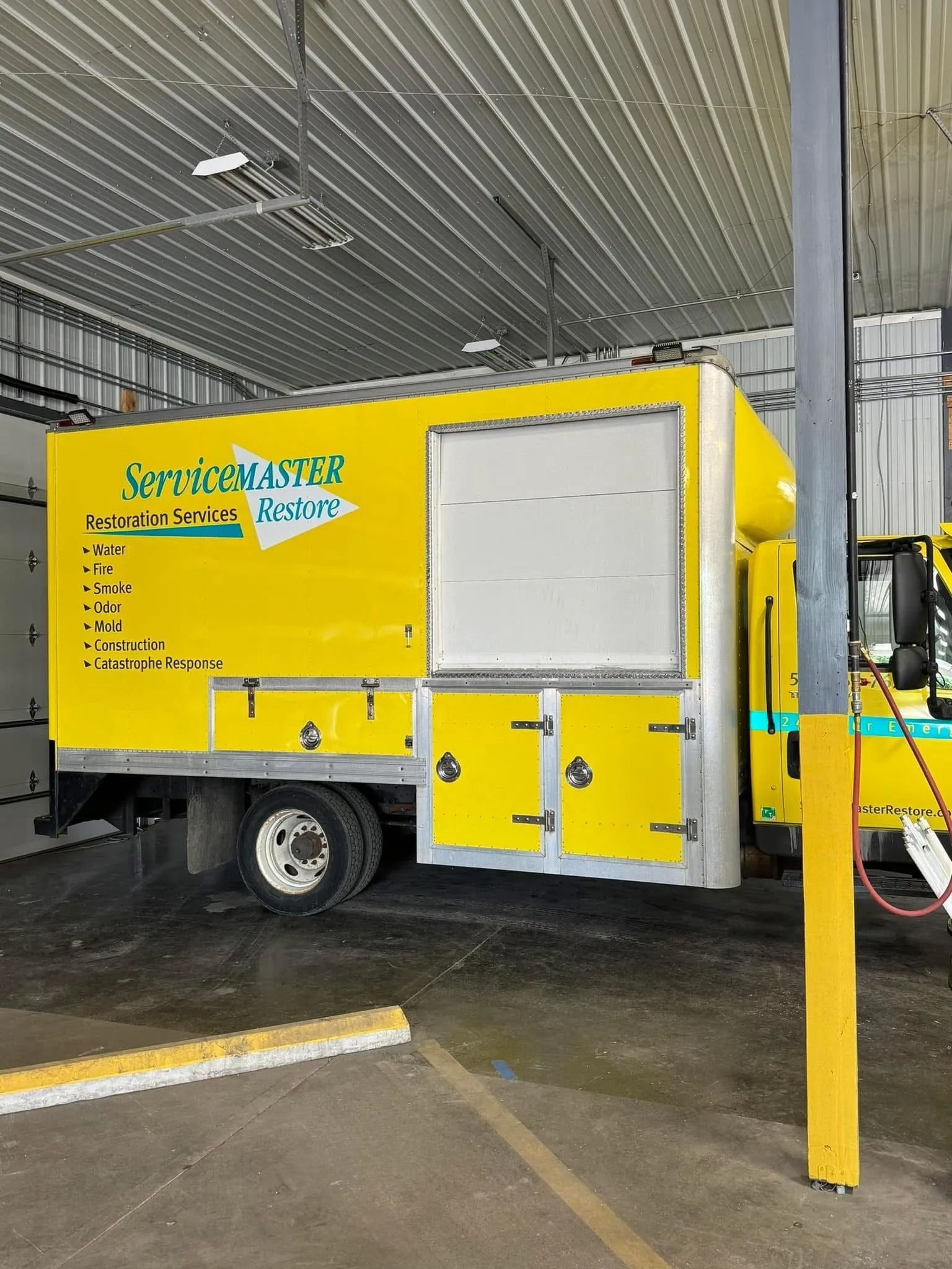 Yellow and white service truck parked inside a building. The truck has large doors and the side reads 