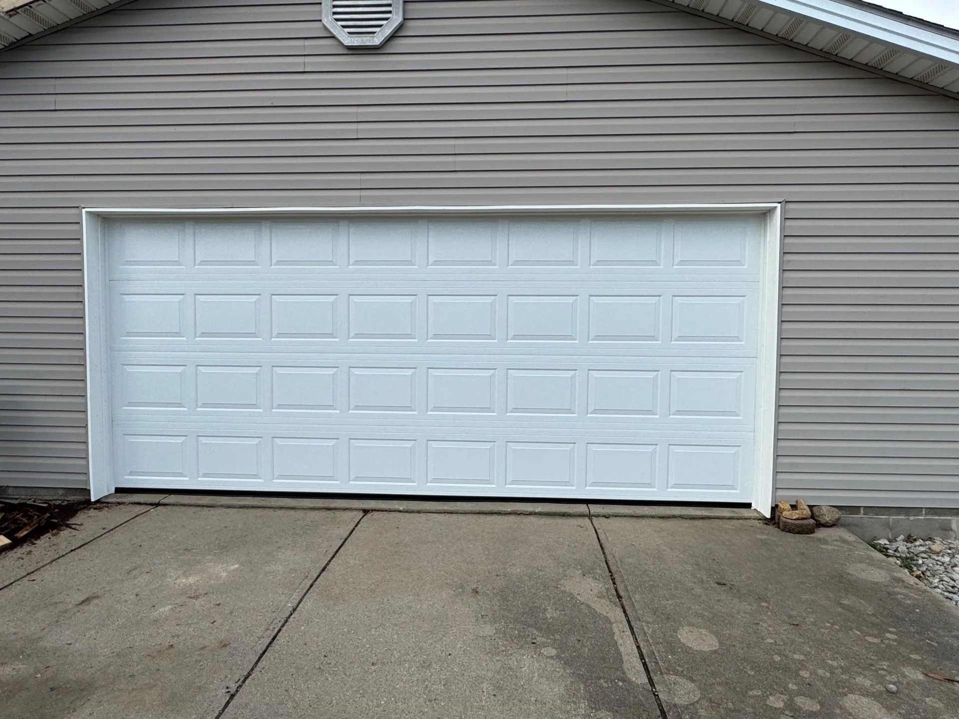 White garage door on a gray house with a concrete driveway.