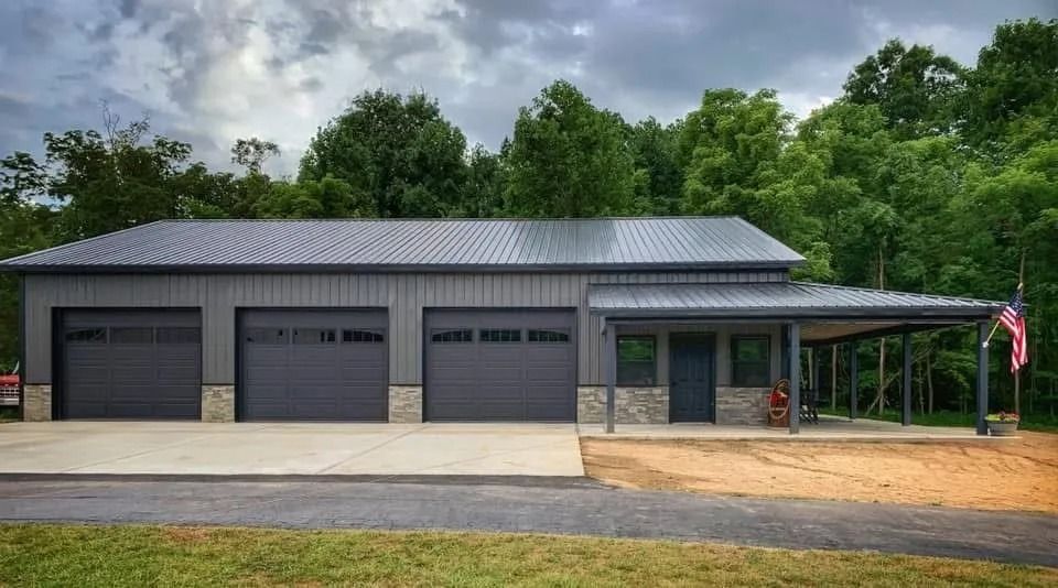 Gray metal garage with three bays, porch, and a flag, set against a wooded backdrop.