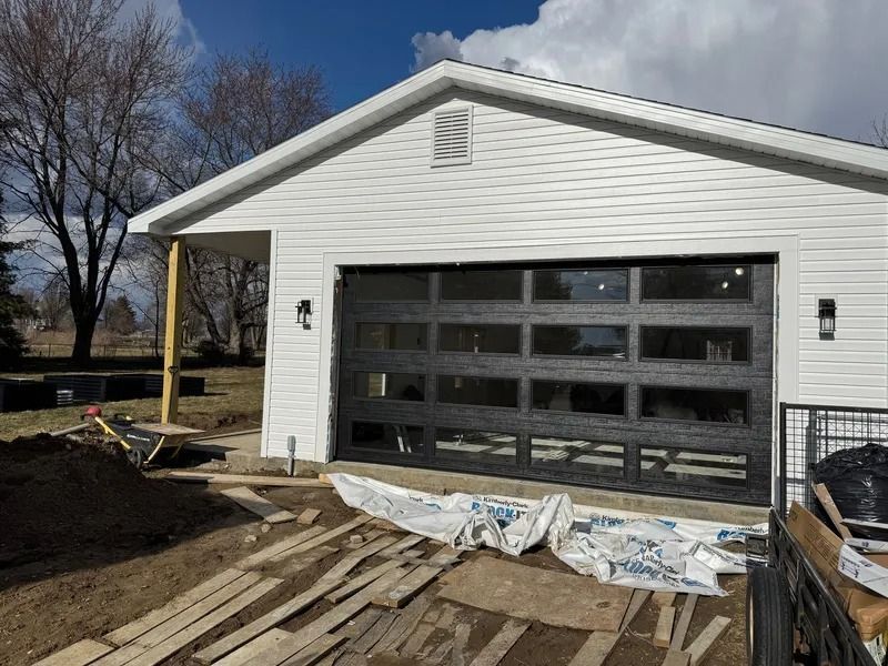 Black garage door with glass panels on a white building under construction.