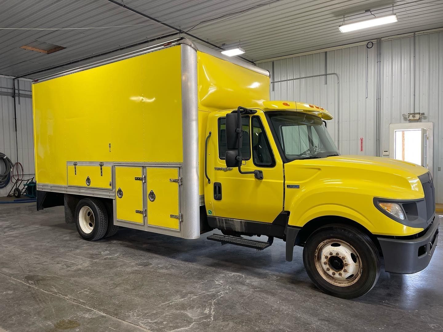 Yellow box truck inside a garage, with side storage compartments.