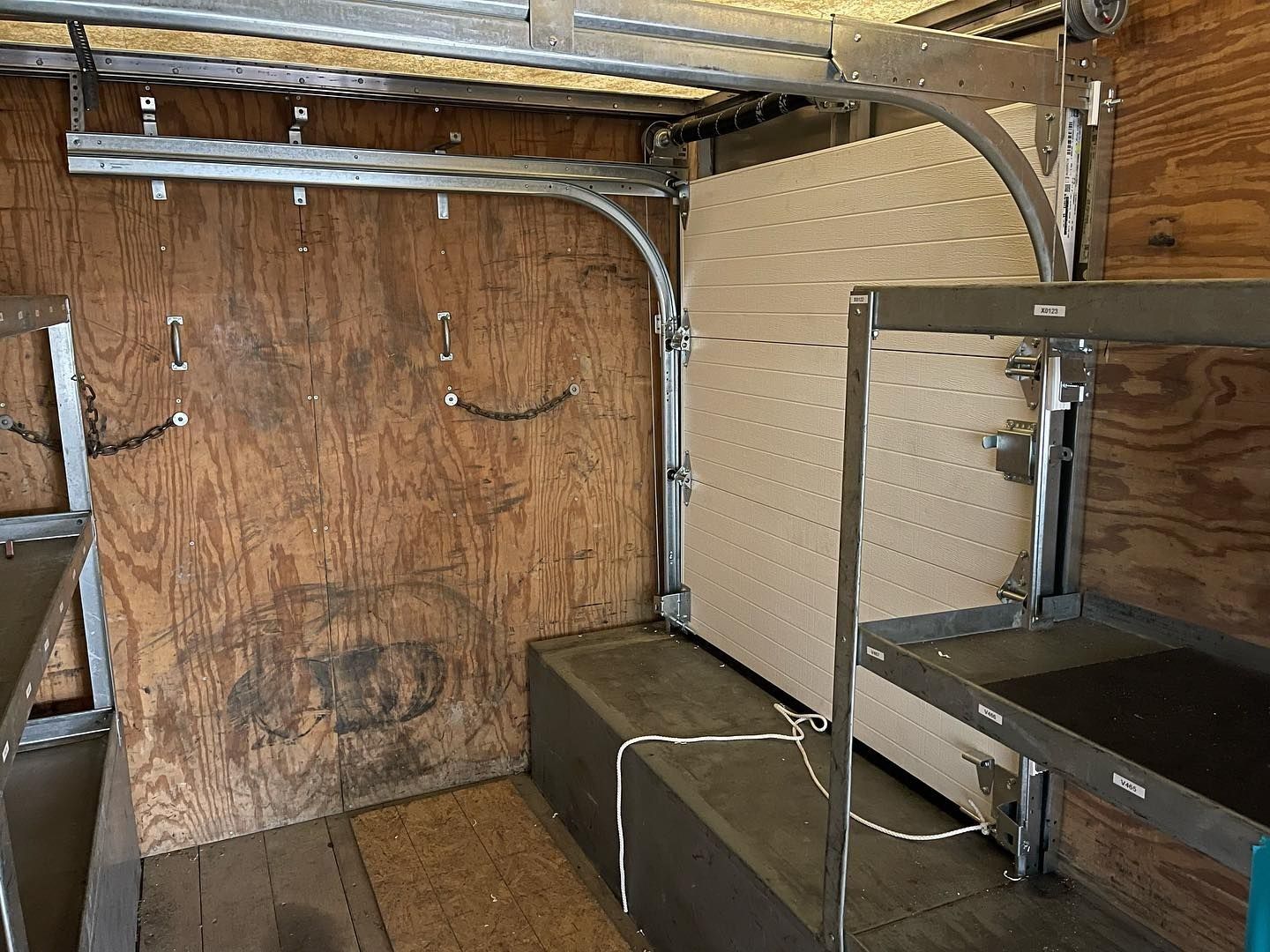 Interior of a truck with a roll-up door, metal shelving, and wooden walls.