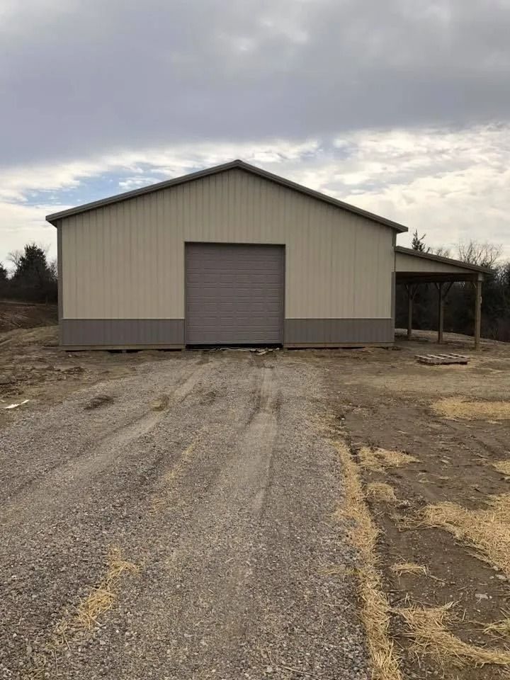 Beige and brown metal barn with a gravel driveway and cloudy sky.