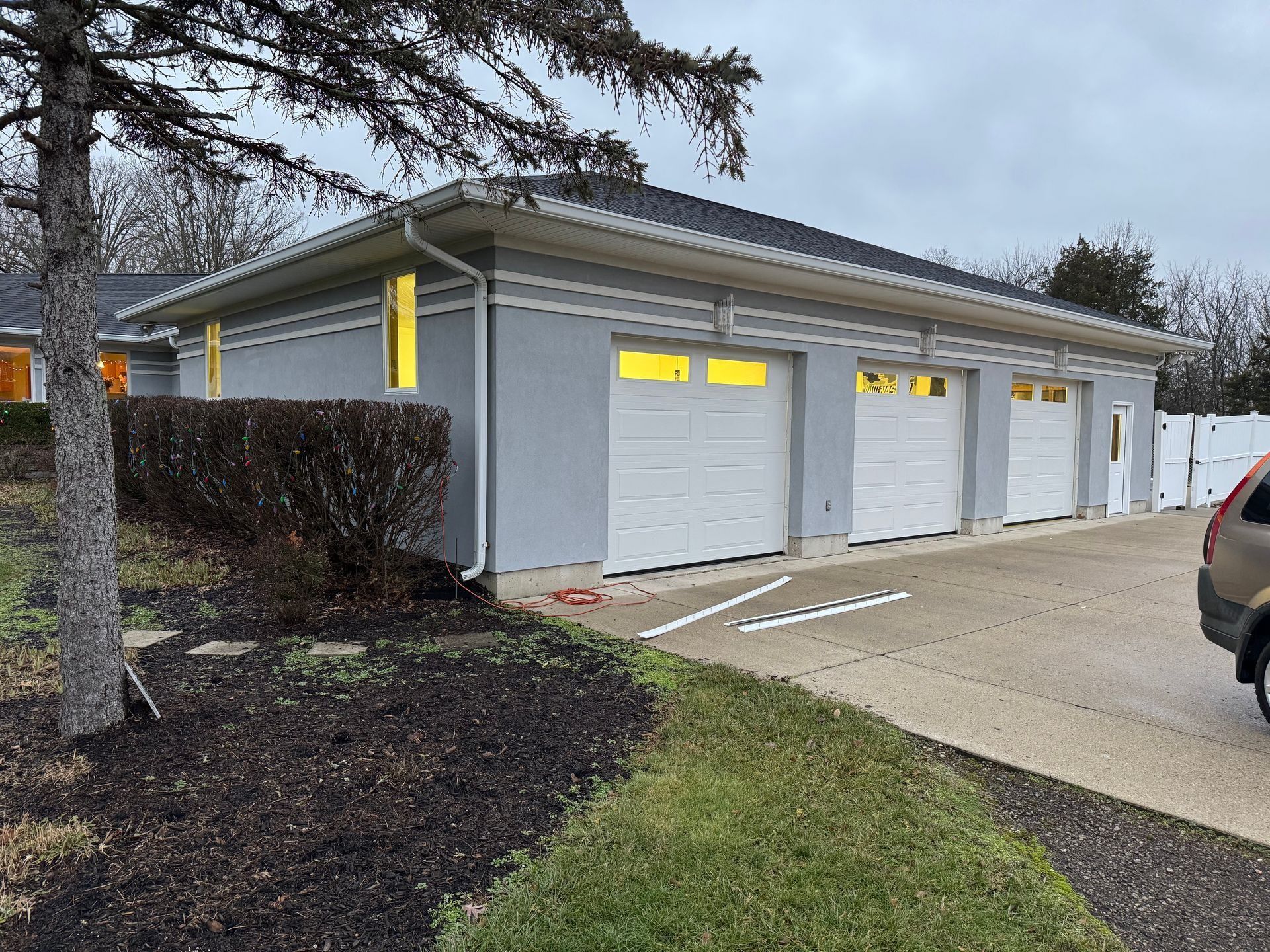 Three-car garage with white doors, light gray stucco walls, and a dark roof.