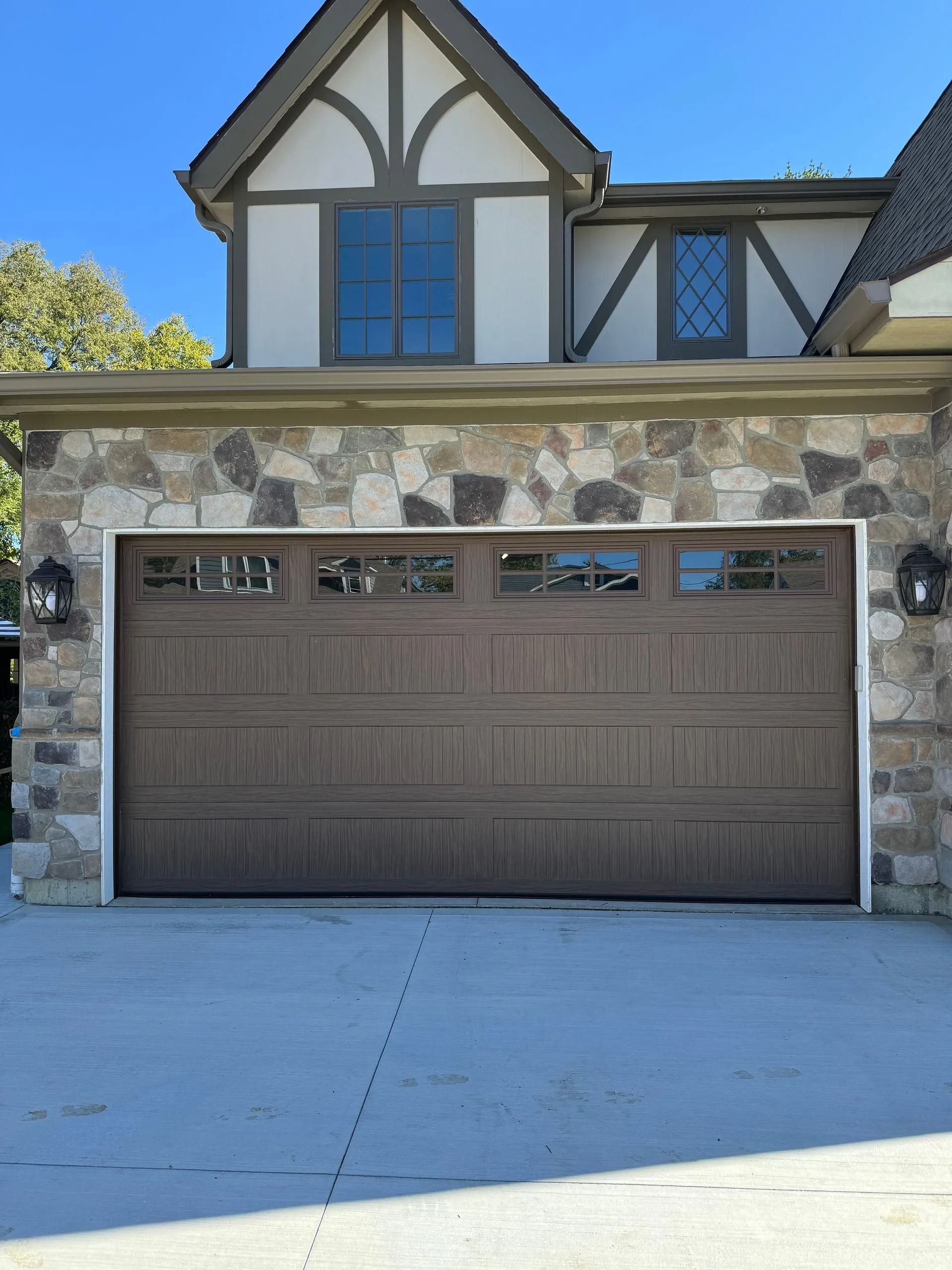 Brown garage door on a stone and stucco house. Clear sky.