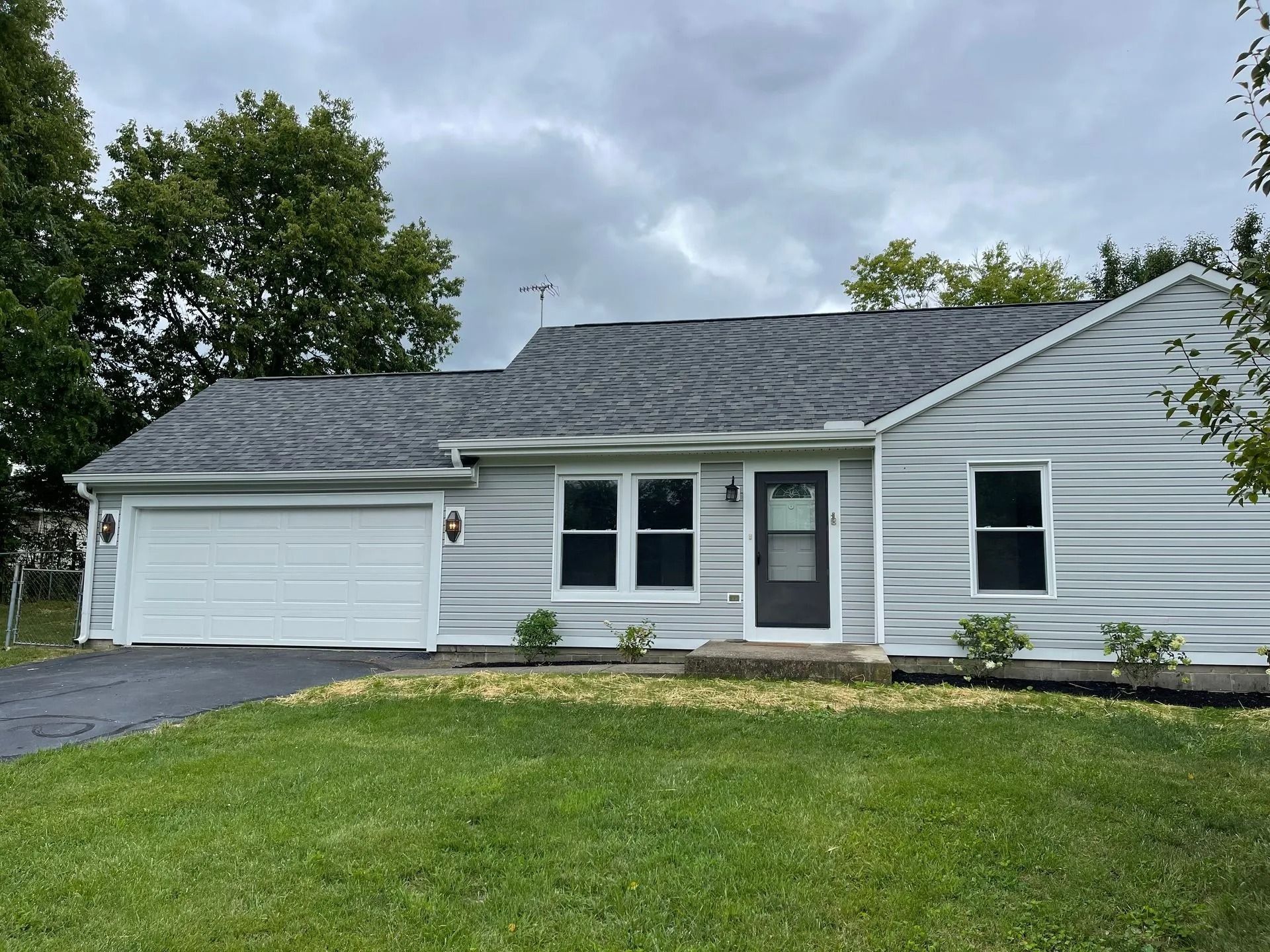 House with gray siding and roof, white garage door, and green lawn under cloudy sky.