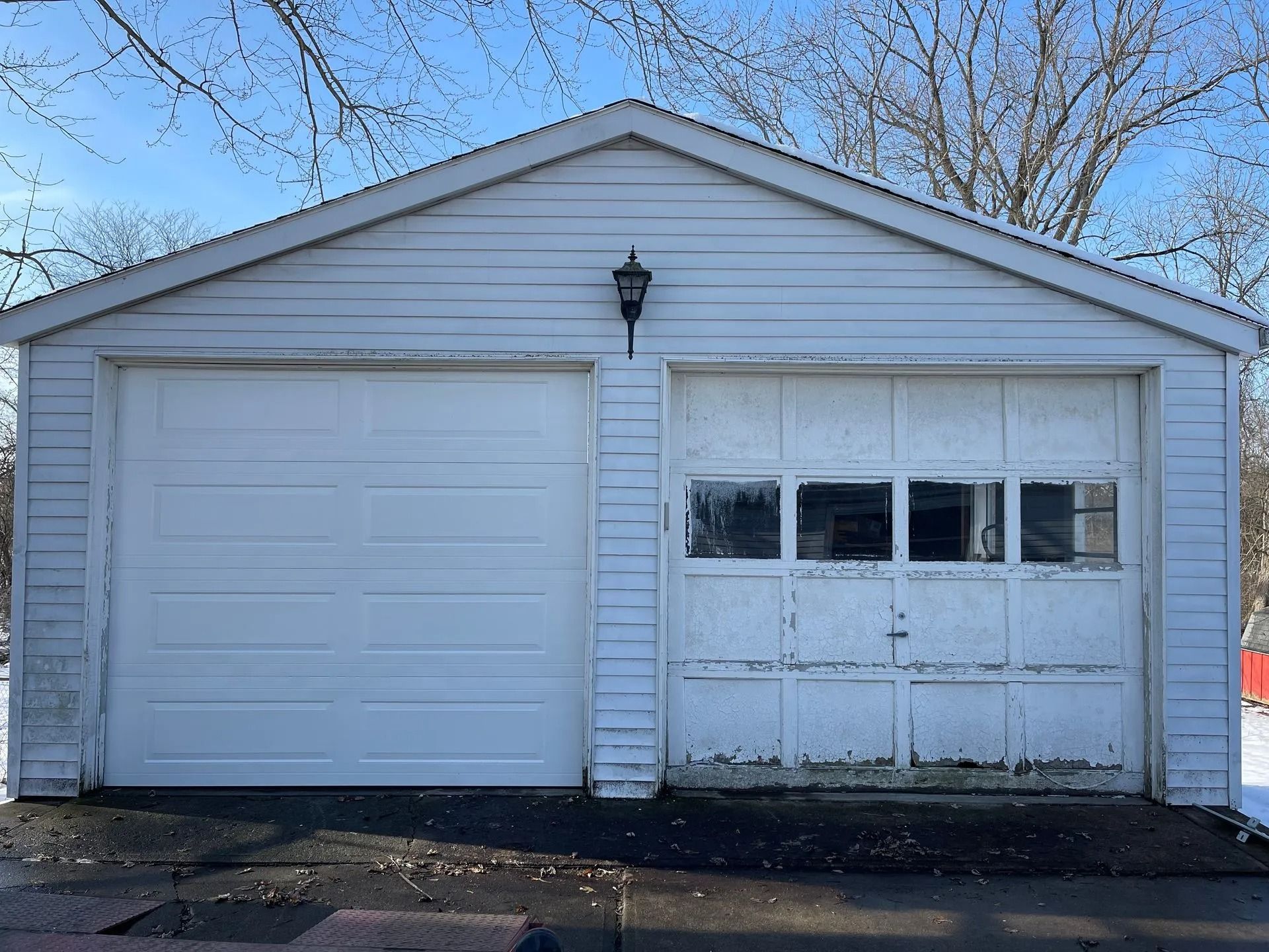 White, two-car garage with weathered, paneled door on right. One door is solid, the other has windows.