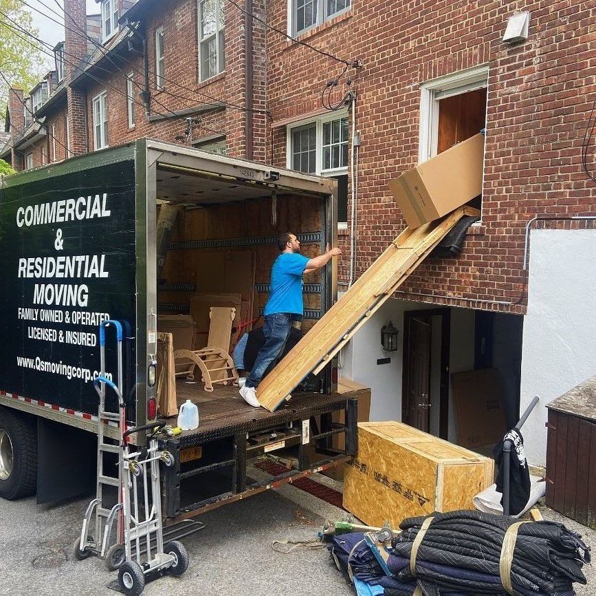 A commercial and residential moving truck is parked in front of a brick building