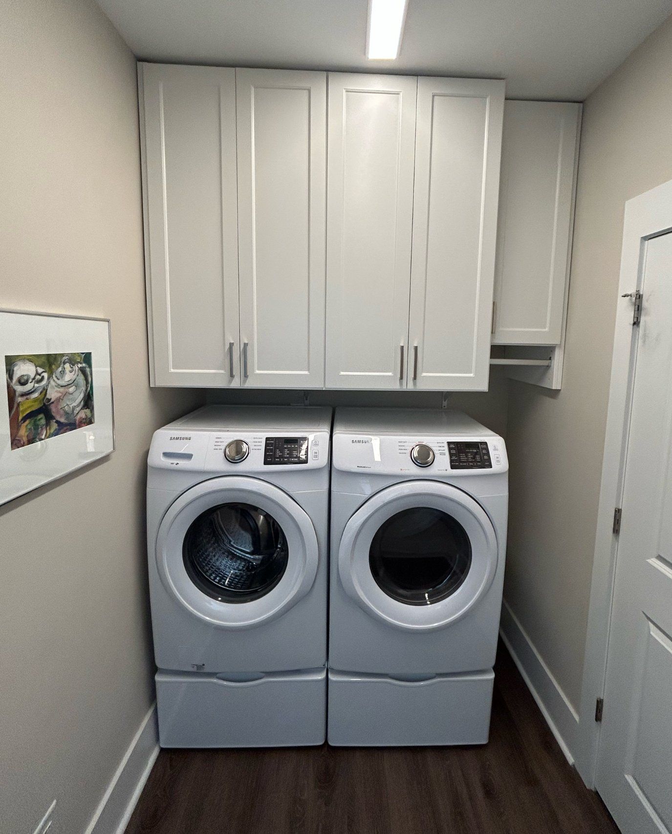 A laundry room with two washers and dryers and white cabinets.