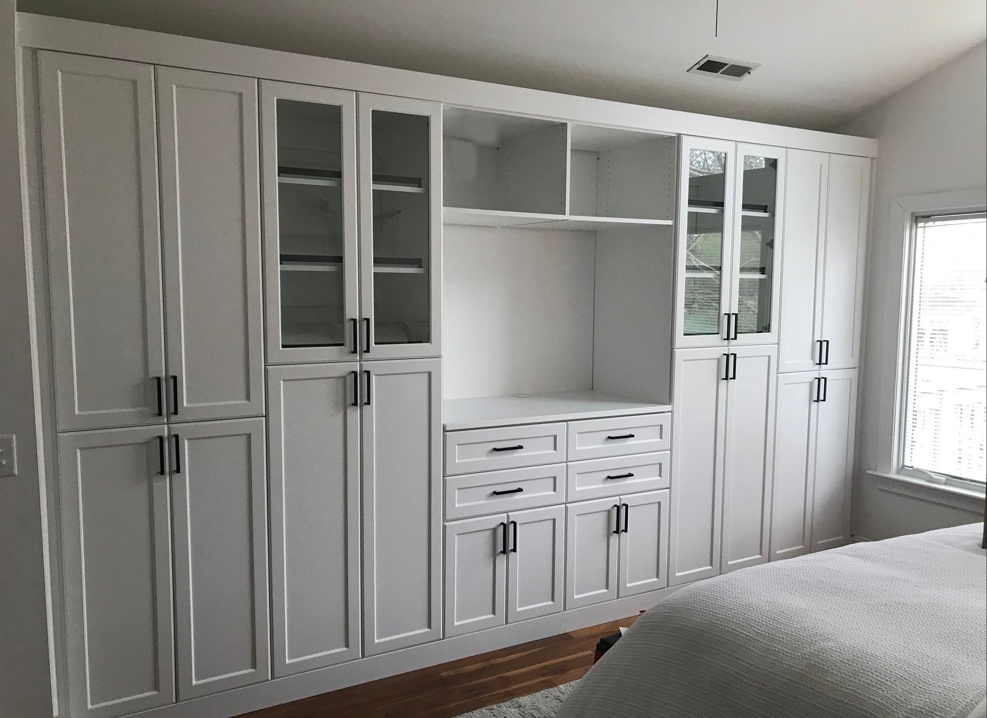 A bedroom with a large wall of white cabinets and drawers.