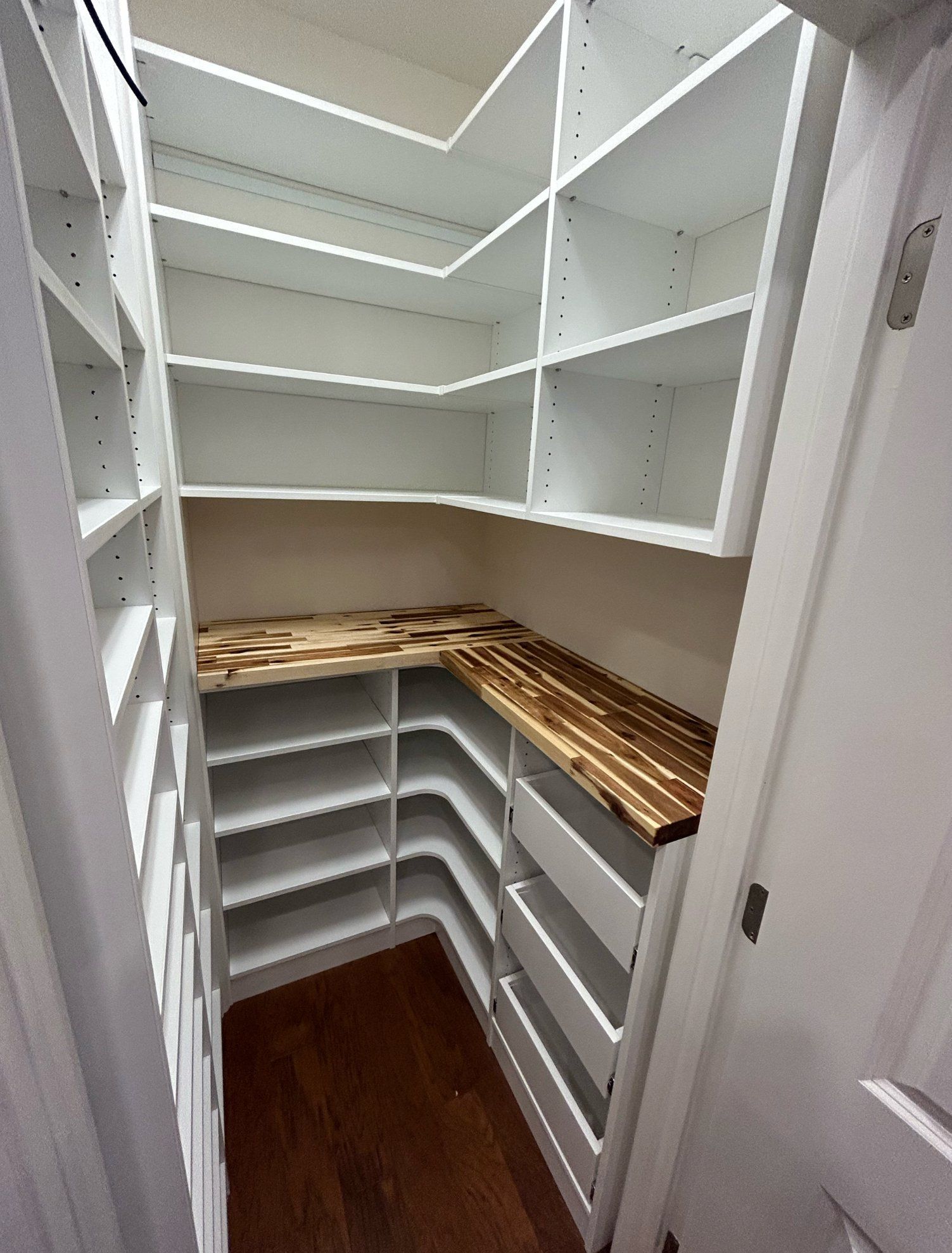 A small closet with white shelves and a wooden counter top