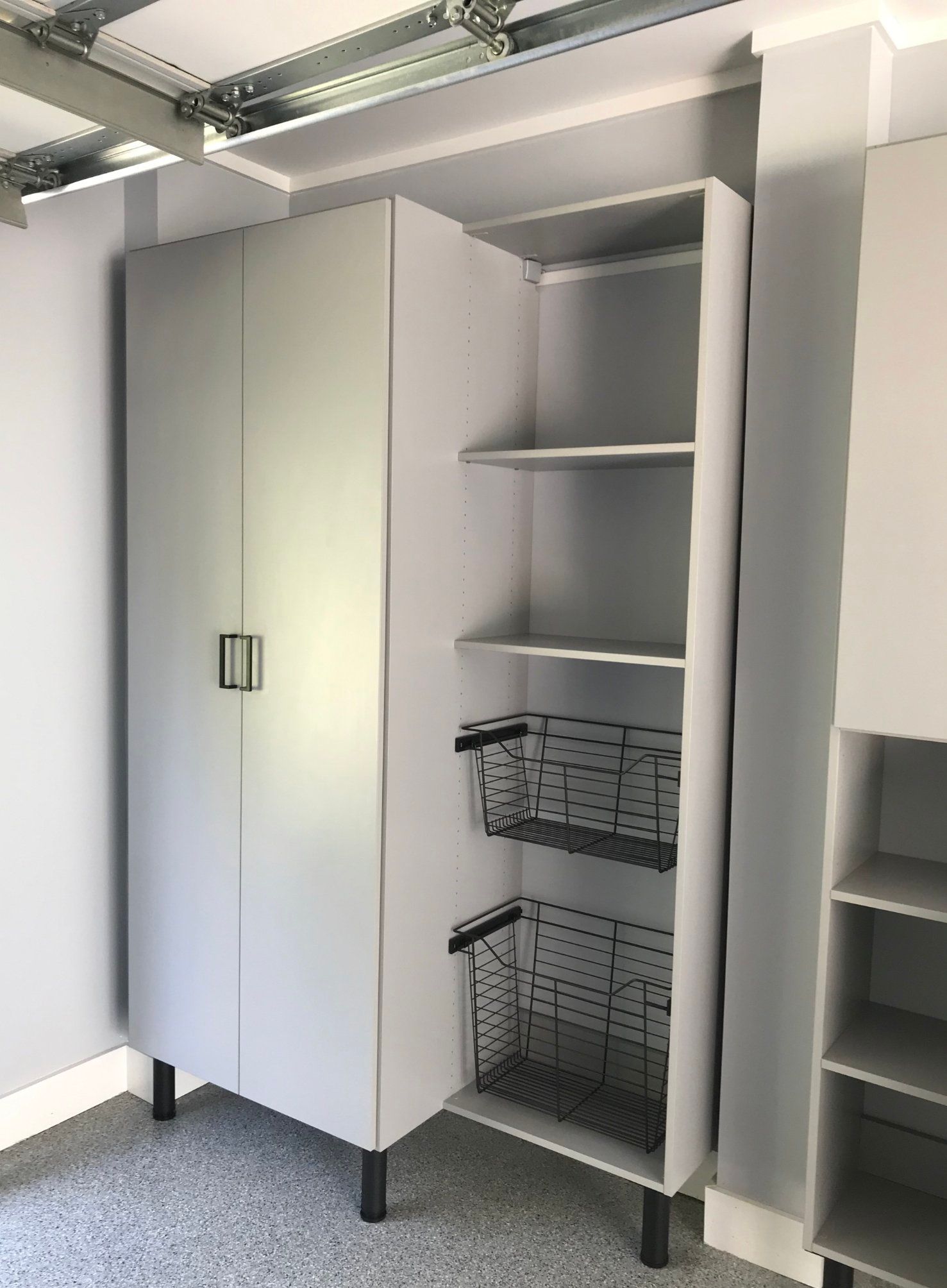 A white cabinet with shelves and baskets in a garage.
