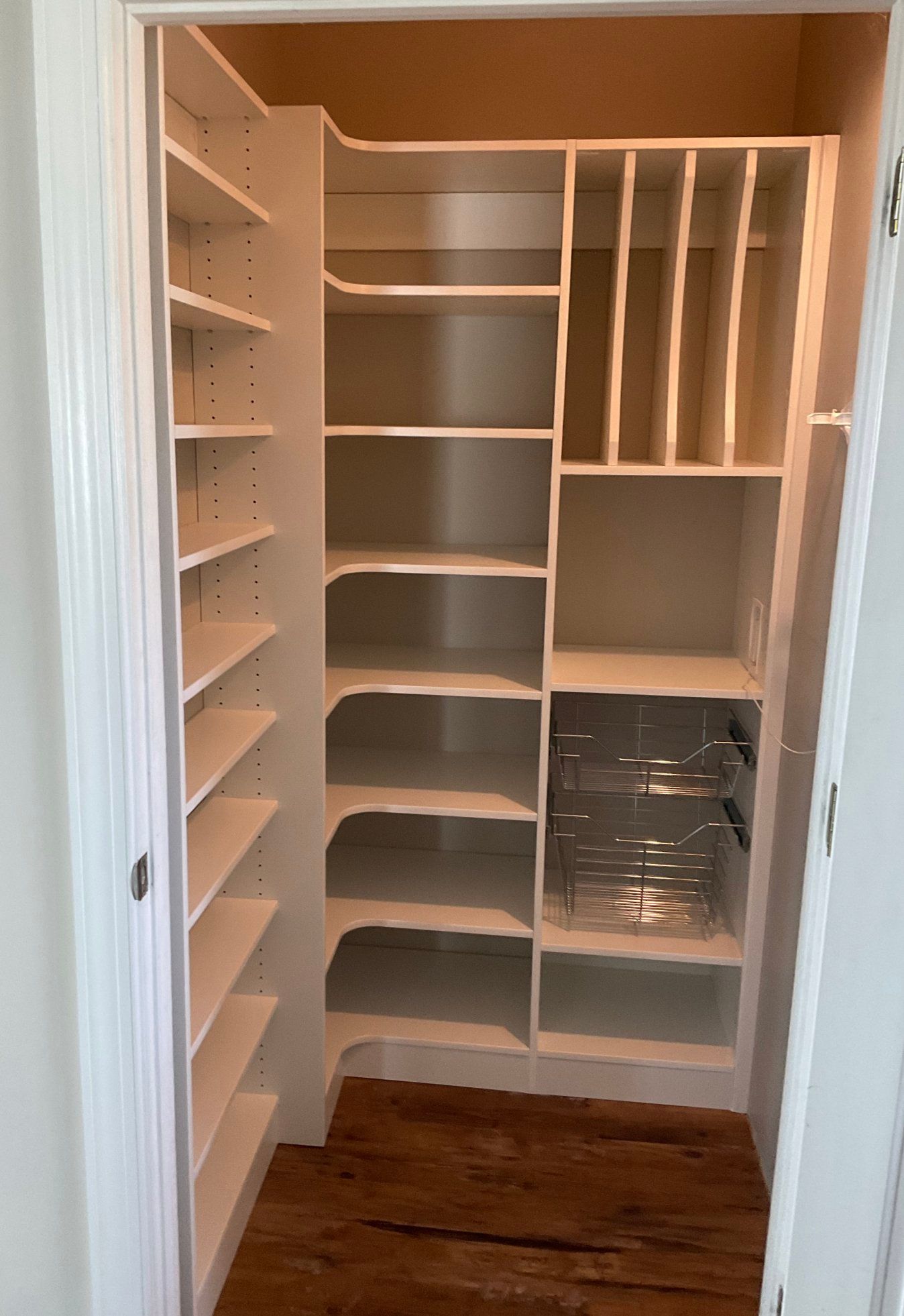 A walk in closet with white shelves and a wooden floor.