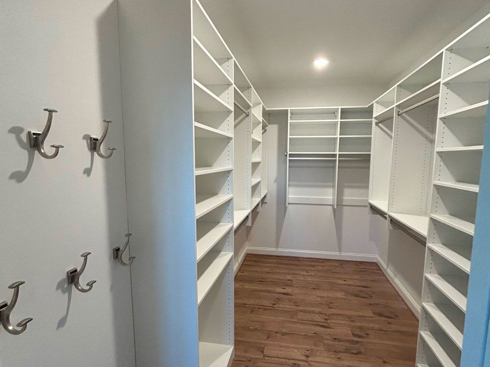 A walk in closet with lots of shelves and hooks on the wall.
