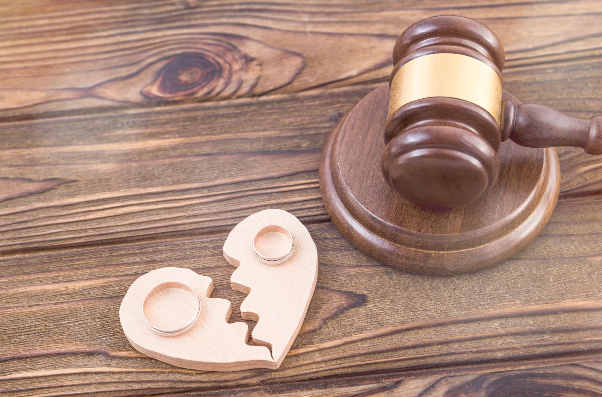 Broken heart with wedding rings, beside a judge's gavel on a wooden surface.