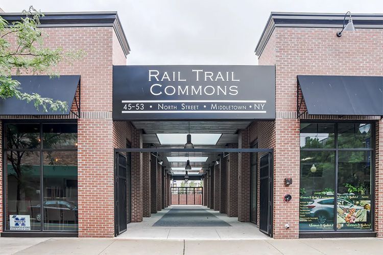Brick storefront entrance sign reading 'Rail Trail Commons' with a covered walkway between buildings