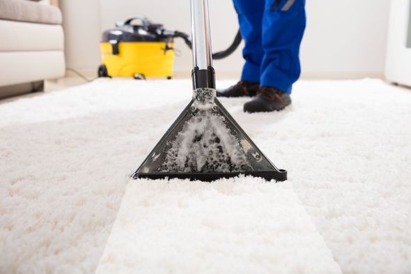 Person in blue overalls vacuuming a white carpet with a yellow and black vacuum cleaner.