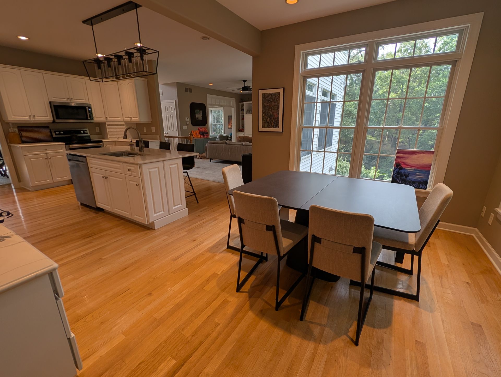 A kitchen with light wood floors, a table with four chairs, and a large window.