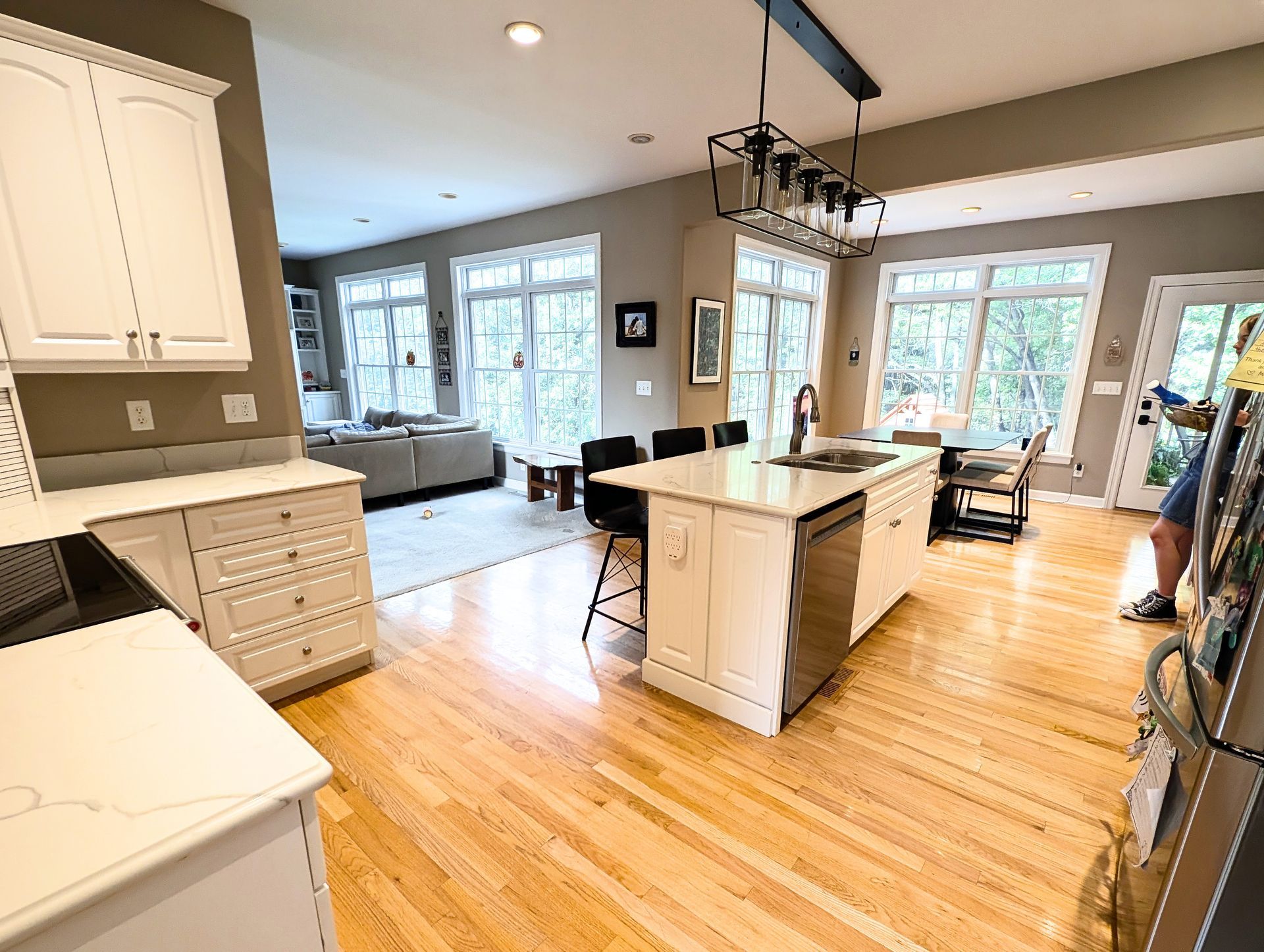 Open-concept kitchen with white cabinets, island, hardwood floors, and a view to a living room.