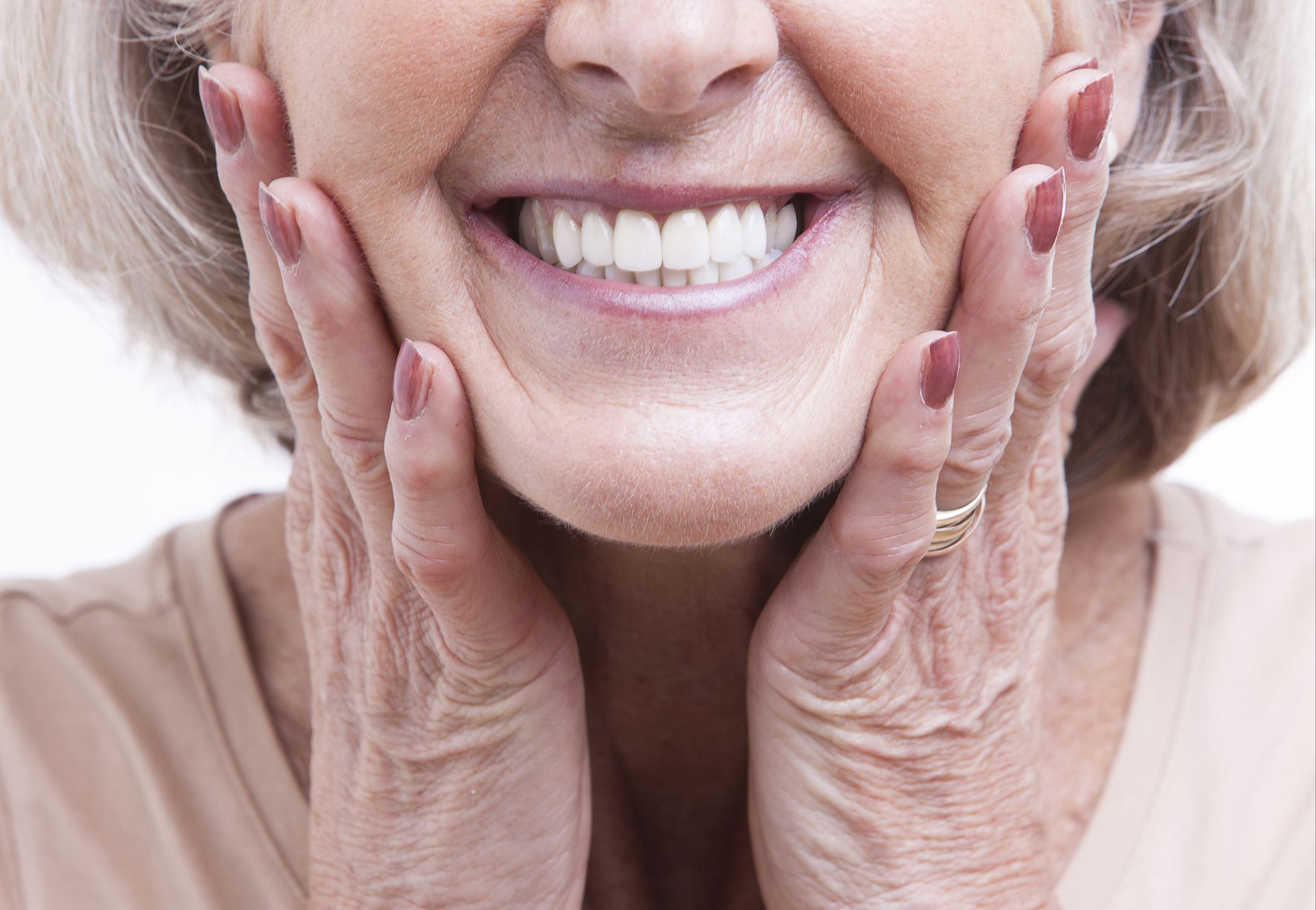 Close-up of an older woman smiling and holding her face, showing a full set of clean, healthy teeth, possibly dentures.