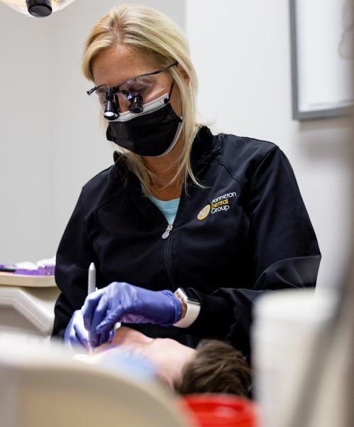 A woman wearing a mask and gloves is working on a child 's teeth